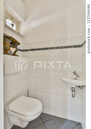 A clean and contemporary bathroom featuring white tiles, a modern toilet, and elegant decor. Perfectly captures minimalist design with functionality. 125504446