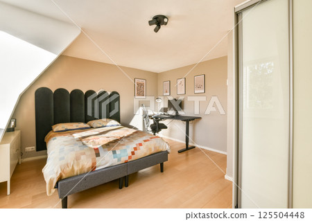 A contemporary bedroom featuring a stylish bed with colorful bedding, a dark accent wall, and a functional workspace, showcasing modern interior design elements. 125504448