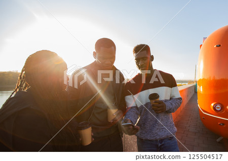 African american friends looking smartphone while standing by river. Concept of technology, friendship, real life connection. African american friends looking smartphone while standing by river. Concept of technology, friendship, real life connection. 125504517