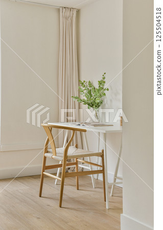 A bright and airy dining area showcasing a wooden chair and table adorned with a simple vase of green plants, highlighting minimalistic design and natural light. A bright and airy dining area showcasing a wooden chair and table adorned with a simple vase of green plants, highlighting minimalistic design and natural light. 125504518