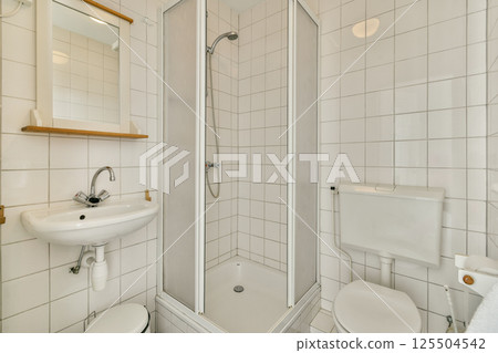 Compact bathroom featuring a sleek shower enclosure, minimalist sink, and tiled walls, emphasizing functionality and contemporary design aesthetics. 125504542