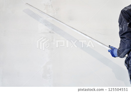 An unrecognizable man holds a metal rule for leveling plaster on walls. High quality photo 125504551