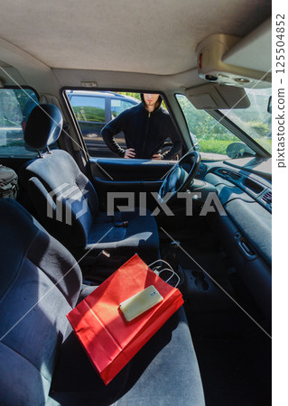 Burglar thief stealing smartphone and bag from car Burglar thief stealing smartphone and bag from car 125504852