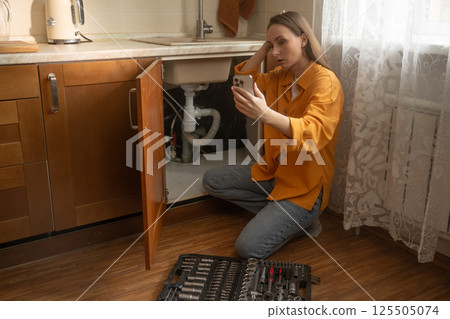 Woman calls repair service for urgent kitchen sink drain issue in residential home during afternoon hours Woman calls repair service for urgent kitchen sink drain issue in residential home during afternoon hours 125505074