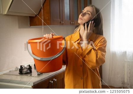 Woman calling for help holding bucket under water leak in kitchen Woman calling for help holding bucket under water leak in kitchen 125505075