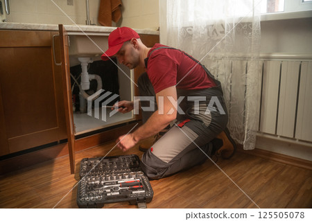 Plumber fixing leaky sink in kitchen Plumber fixing leaky sink in kitchen 125505078