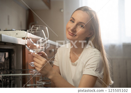 Housewife unloading clean wine glasses from dishwasher in kitchen Housewife unloading clean wine glasses from dishwasher in kitchen 125505102
