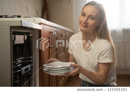 Woman unloading clean dishes from dishwasher in modern kitchen 125505103