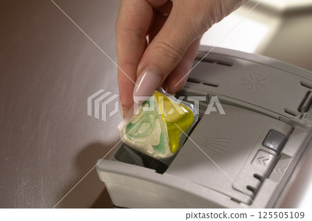 Woman placing laundry detergent pod into washing machine Woman placing laundry detergent pod into washing machine 125505109