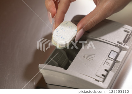 Housewife placing laundry detergent tablet into washing machine 125505110