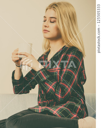 Teenage woman sitting on sofa with mug Teenage woman sitting on sofa with mug 125505333
