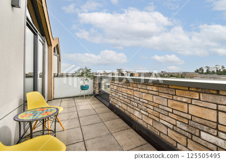 A contemporary balcony featuring a colorful table and chairs overlooking a city skyline under a blue sky with clouds. 125505495