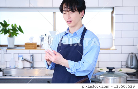 Image of a man thinking while looking at his smartphone in the kitchen Image of a man thinking while looking at his smartphone in the kitchen 125505529