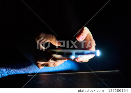 A Hand Gripping a Smartphone in a Low Light Environment, Showcasing Modern Technology and Design 125506164