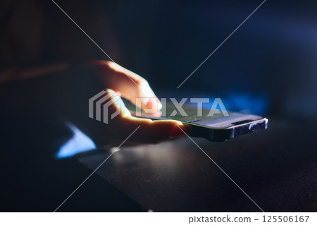 A Hand Gripping a Smartphone in a Low Light Environment, Showcasing Modern Technology and Design 125506167