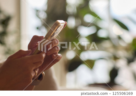 A person is comfortably using their smartphone while sitting in a cozy, relaxed environment 125506169