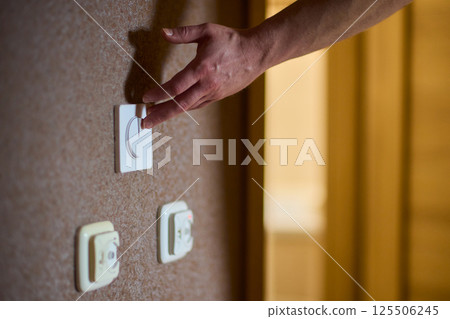 A hand reaches for the light switch in a cozy room, adding warmth and brightness 125506245
