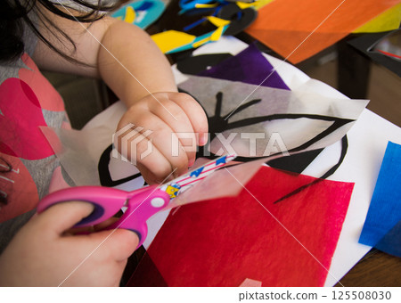 Small child makes paper butterfly for mother's day or birthday. Simple and nice gift idea. Scissors, color paper flowers templates, butterfly on a wooden table. Small child makes paper butterfly for mother's day or birthday. Simple and nice gift idea. Scissors, color paper flowers templates, butterfly on a wooden table. 125508030
