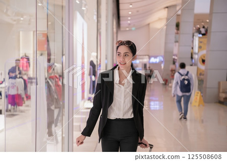 A confident woman in a suit walking through a modern shopping mall, exuding professionalism and style. A confident woman in a suit walking through a modern shopping mall, exuding professionalism and style. 125508608