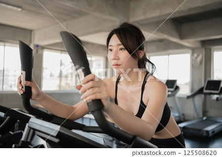 A young woman exercises on an elliptical machine in a bright gym, focusing intensely on her workout routine. A young woman exercises on an elliptical machine in a bright gym, focusing intensely on her workout routine. 125508620