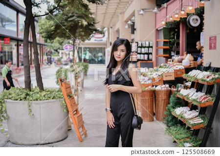 A stylish woman poses confidently in an urban market filled with fresh produce and vibrant flowers. 125508669
