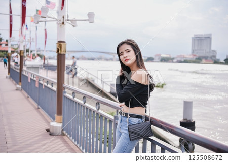 A young woman poses confidently by the river, showcasing modern fashion and vibrant city life. A young woman poses confidently by the river, showcasing modern fashion and vibrant city life. 125508672