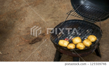 Rustic Potatoes Cooking on a Charcoal Grill with Open Lid for Summer BBQ Gatherings 125509746