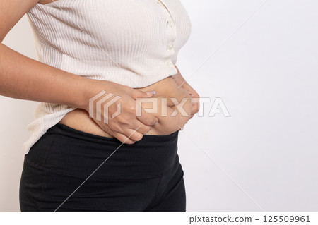 Overweight woman hand pinching excessive belly fat on gray background, Healthy concept Overweight woman hand pinching excessive belly fat on gray background, Healthy concept 125509961