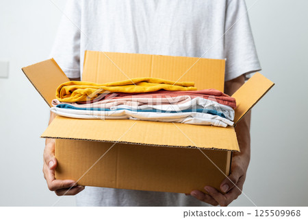 Donation Concept, man holding clothes with donate box in white background room. 125509968
