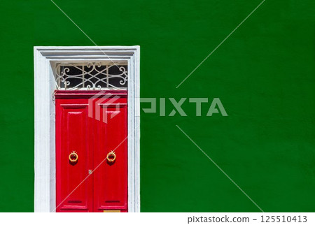 Green wall of a residential building with a red door in a white wooden frame 125510413