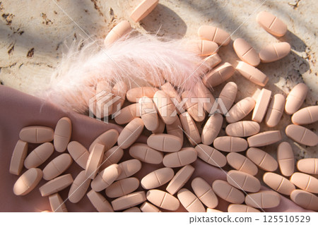 Pills or vitamins on the natural wood background with pink silk fabric and feather in summer day. Top view.  125510529