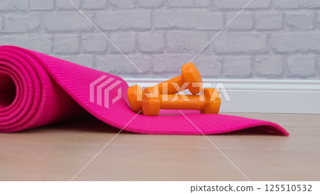 Two orange dumbbells on a pink yoga mat in fitness studie. A tools for training, sport and activity in summer time. Two orange dumbbells on a pink yoga mat in fitness studie. A tools for training, sport and activity in summer time. 125510532