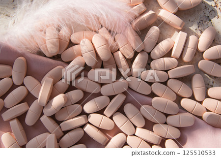 Pink pills or vitamins on the natural wood background with pink silk fabric and feather in summer day. Top view.  125510533