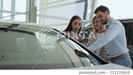Happy family couple talking to car dealer in dealership discussing automobiles looking at new model. Concept of car shopping, buying, and dealership. 125510920