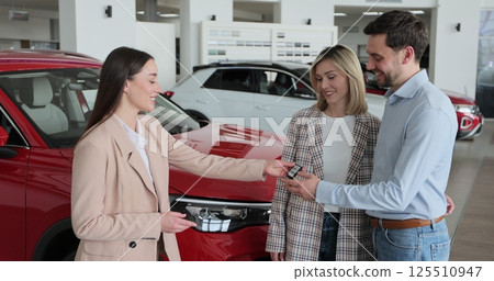 Young couple buying new car in car dealership. Saleswoman giving car keys to new car happy couple family buyers. Auto business concept. Young couple buying new car in car dealership. Saleswoman giving car keys to new car happy couple family buyers. Auto business concept. 125510947