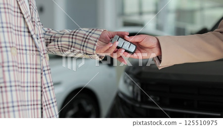Close up woman hand gives a car keys to buyer woman hand in car dealership close up. Concept of car shopping, buying, and dealership. 125510975