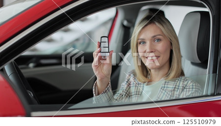 Young woman showing key to new car. Auto business concept. Woman holding car keys at the dealership salon. 125510979