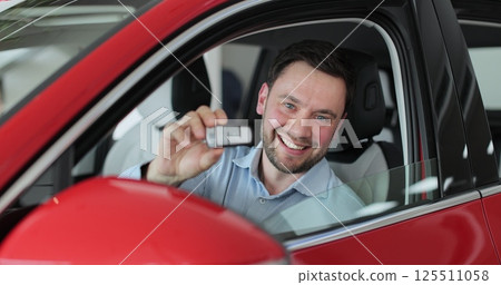 Sales manager handing over the keys to man in the car. Young man showing key to new car. Man holding car keys at the dealership salon. Auto business concept. 125511058