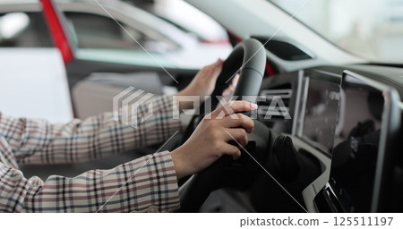 Close up hands young woman auto driver car owner holding steering wheel buy new automobile dealership inside vehicle. Concept of car shopping, buying, and dealership. 125511197
