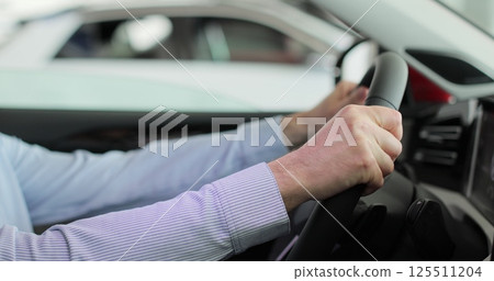 Close up young man auto driver car owner holding steering wheel buy new automobile dealership inside vehicle. Concept of car shopping, buying, and dealership. 125511204