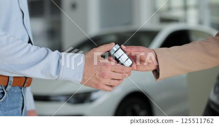 Close up woman hand gives a car keys to man hand in car dealership close up. Concept of car shopping, buying, and dealership. Close up woman hand gives a car keys to man hand in car dealership close up. Concept of car shopping, buying, and dealership. 125511762