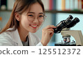 A smiling female scientist adjusts a microscope in a lab setting. 125512372