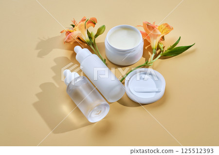 Several cosmetics in jars with lily flowers on a beige background. Several cosmetics in jars with lily flowers on a beige background. 125512393
