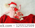 A cute baby in a Santa hat with a big bubo covered with a red knitted blanket hugging a snowman toy on a white background. 125512509