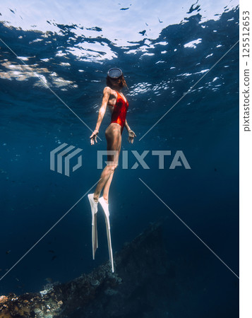 Woman freediver swims underwater in blue sea. 125512653