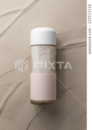 Moisturizing cosmetic milk in glass packaging on sand, empty label, minimalist design 125513118