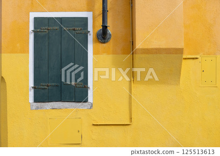 Yellow textured wall with green closed shutters in Burano Italy 125513613