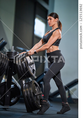 fit woman is focused on lifting heavy weights in contemporary gym. She showcases strength and determination while exercising her core and arms. atmosphere is energetic and motivating. 125513692