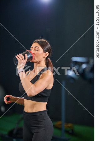 Focused woman in athletic wear hydrates drink while exercising in training environment. setting emphasizes health and fitness. Focused woman in athletic wear hydrates drink while exercising in training environment. setting emphasizes health and fitness. 125513699