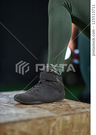 person demonstrates strength training techniques while wearing specialized footwear on raised platform in gym setting. focus is on grip and design of shoes essential for performance. 125513711